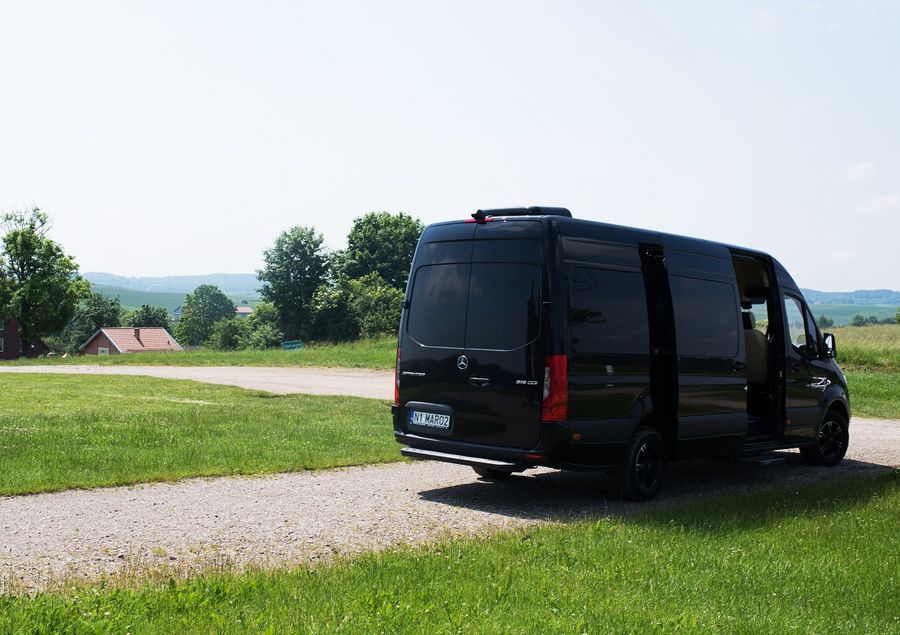 Mercedes Sprinter VIP z otwartymi drzwiami i widocznym jasnym wnętrzem — zdjęcie samochodu zrobione w Gietrzwałdzie, w tle tabliczka z nazwą miejscowości
