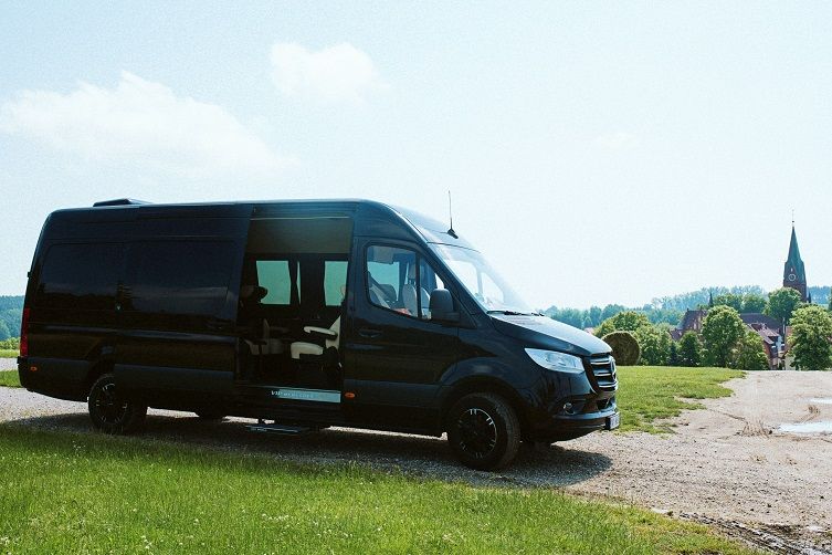 Bus z kierowcą na wyjazdy grupowe — zdjęcie samochodu Mercedes Sprinter VIP ze skórzanymi fotelami zrobione w Gietrzwałdzie, z wieżą bazyliki w tle